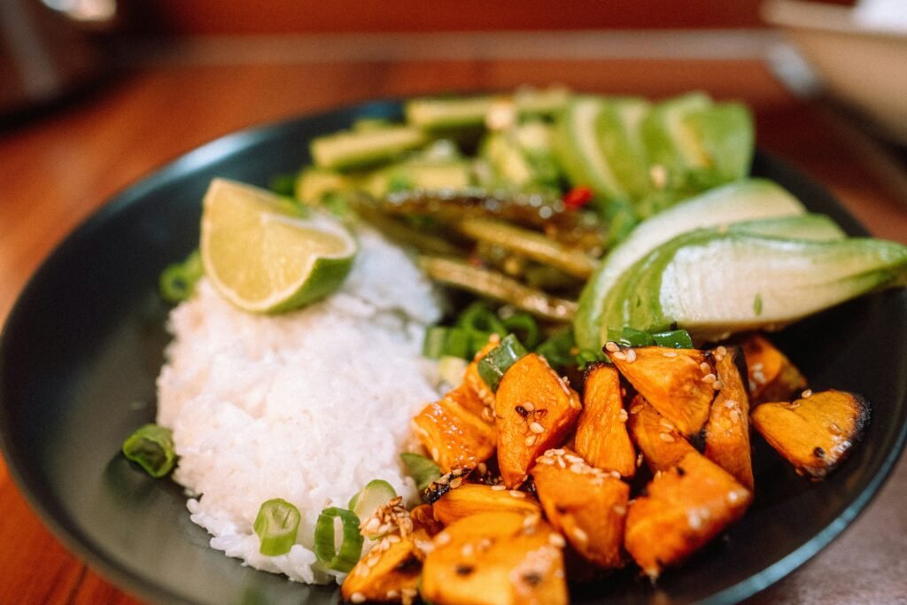 Plate of white rice paired with vegetables, lime, and roasted sweet potato